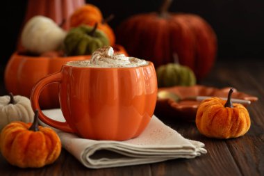 Balkabağı şeklinde bir kupada, sonbahar dekoruyla çevrili, krema ve baharatlı, kabak şeklinde bir latte..