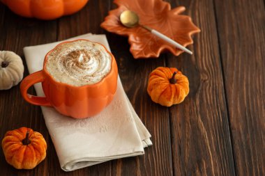 Balkabağı şeklinde bir kupada, sonbahar dekoruyla çevrili, krema ve baharatlı, kabak şeklinde bir latte..