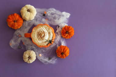 Cadılar Bayramı temalı düz yatış, balkabaklı latte, dekoratif balkabakları ve mor arka planda örümcek ağları..