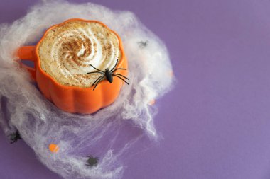 Cadılar Bayramı temalı düz yatış, balkabaklı latte ve mor arka planda örümcek ağları..