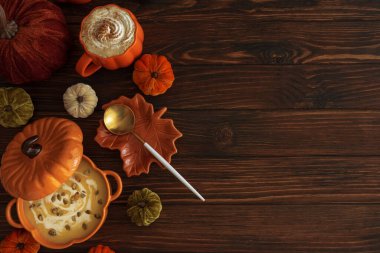 Balkabağı şeklindeki bir kâsede balkabağı çorbası, balkabağı latte, kızarmış ekmek ve koyu ahşap masada şenlikli bir dekor ile sonbahar yemeği. Üst Manzara. Boşluğu kopyala