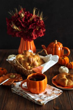Sonbahar çay seti pişmiş çörekleri sepsiyona, balkabağı şeklindeki çaydanlığa ve ahşap bir masada kupaya..