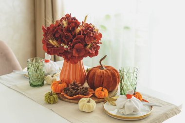 Süslü balkabakları, mumlar ve beyaz ahşap masa üzerindeki iplik ışıkları ile Şükran Günü sofrası.