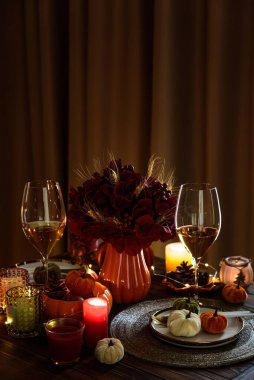 Süslü balkabaklarıyla Şükran Günü sofrası, mumlar ve sicim ışıkları koyu ahşap masa üzerinde.