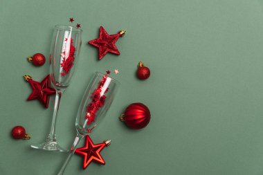 Kırmızı Noel süsleriyle şampanya flütleri ve yeşil arka planda kurdele