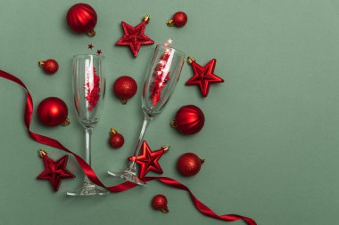 Kırmızı Noel süsleriyle şampanya flütleri ve yeşil arka planda kurdele