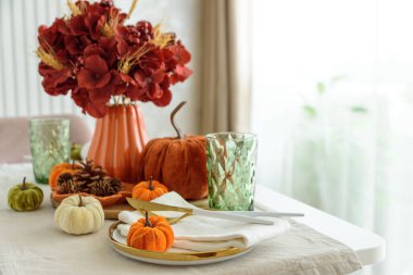 Süslü balkabakları, mumlar ve beyaz ahşap masa üzerindeki iplik ışıkları ile Şükran Günü sofrası.