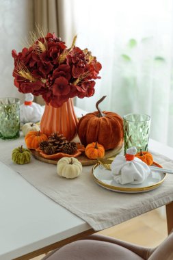 Süslü balkabakları, mumlar ve beyaz ahşap masa üzerindeki iplik ışıkları ile Şükran Günü sofrası.