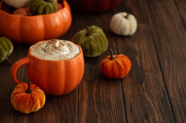 Balkabağı şeklinde bir kupada, sonbahar dekoruyla çevrili, krema ve baharatlı, kabak şeklinde bir latte.