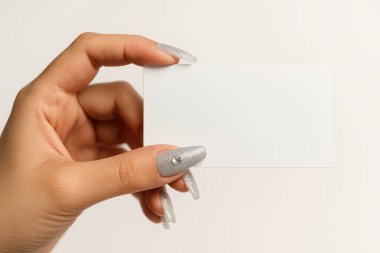 Beyaz arka planda süslü tırnakları olan bir kadının elindeki beyaz kartvizit.