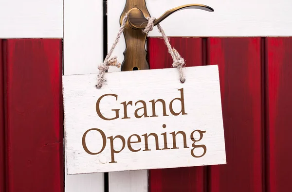 Wooden sign hanging on a door handle with message grand opening
