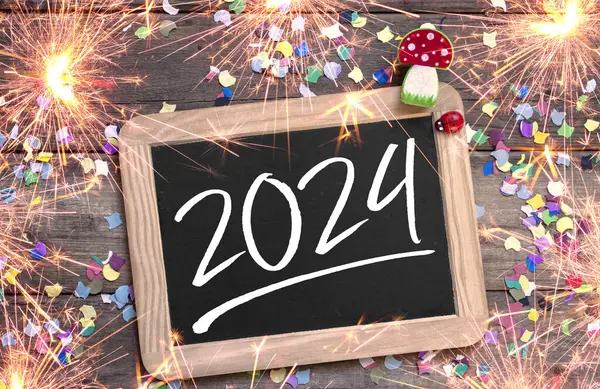 Wooden hang tag and slate with four leaf clover and sparklers with the german words for happy new year - frohes neues jahr 2024 on wooden weathered background
