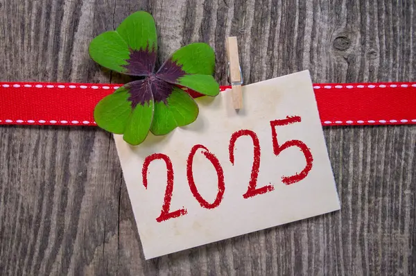 Ahşap askı etiketi ve dört yapraklı yonca ve mutlu yeni yıl için Almanca sözcüklerle kıvılcımlar - ahşap yıpranmış arka planda neue jahr 2025