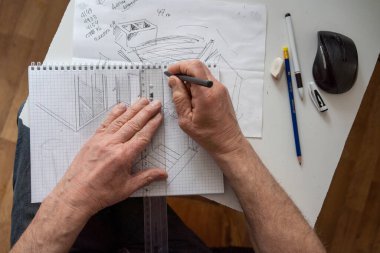 Erkek mimar, bir kağıt parçasına resim çiziyor. Kalem ve cetvelle bir elin üst görüntüsü.