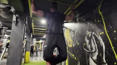 Spor salonunda bir adam yatay çubukta barfiks çekiyor.