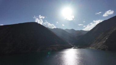  Gölün ve Dağ Majestelerinin sakin yeşil suları, göz kamaştırıcı güneş ışınları, güneşten öpülmüş manzara, ve tüylü beyaz bulutlar ile dramatik gökyüzü, karanlık renkler, ve berrak mavi alan, 