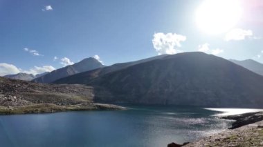 Dağ Gölü Görkemli Siyah ve Yeşil Tepeler, Göz kamaştırıcı Güneş ışınları ile Sakin Yeşil Sular, Güneş Öpen Manzara ve Kabarık Beyaz Bulutlar ile Dramatik Gökyüzü, Koyu Renkler ve Açık Mavi Alan - 4K