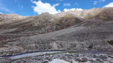 4K Dağ Manzarası, Bereketli Yeşil Çayırların arasından akan Serene Nehri 'nin Yana Dönen Manzarası, Çevrelenmiş Rocky Tepeleri, Dramatik Bulutlar ve Parlak Mavi Gökyüzü Altındaki Güneş Işığı Manzaraları