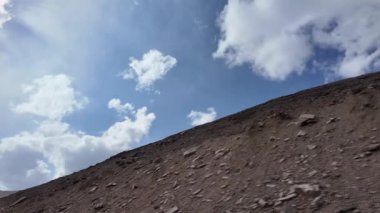 Skyline 'ın nefes kesici görüntüsü Mavi ve Beyaz Gök Altında Dağ Tepeleri' ni gösteriyor. Kara Bulutlar yukarı doğru sürüklenirken, Görkemli bir dağ zirvesi yolun yanına iniyor.