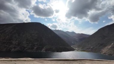 Koyu Yeşil Göl 'ün Sinematik Perspektifi, Karanlık Dağlar tarafından çerçevelenmiş, bir yol kenarından görülen, Mavi ve Yumuşak Bulutlar ile dramatik bir gökyüzü altında,