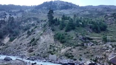 Arkaplanda Görkemli Dağ Sıraları bulunan, yemyeşil çayırlar ve Büyüleyici Evlerle çevrili Akan Nehir 'in Havadan Görünümü. Güneş Işığında Kristal berrak Su Parıltısı, Göz kamaştırıcı Manzara