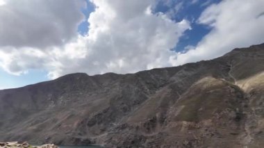 Sükunet Yeşil Göl 'e bakan virajlı bir yoldan bir yan görüntü. Çimenli ve Taşlı Karanlık Dağlar Mavi Gökyüzü Altında Beyaz Yumuşak Bulutlar, Kara Bulut, Yumuşak Güneş Işığı, Yağmur Damlaları