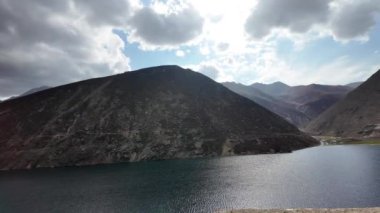 Koyu Yeşil Göl 'ün sinematik hava manzarası, Karanlık Dağlar tarafından çerçevelenmiş, Mavi ve Kabarık Bulutlar ile dramatik bir gökyüzü altında,