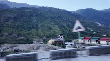 Nehir kenarındaki otellerden oluşan yol kenarı bir sahne. Arka planda yemyeşil dağlara ve ağaçlara yuva yapmış büyüleyici evler. Hepsi dramatik, bulutlarla dolu bir gökyüzünün altında.
