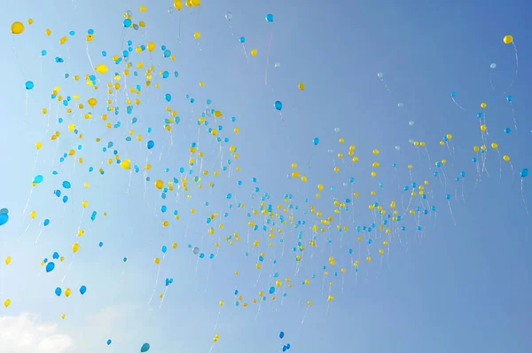 Hundread of balloons in Ukrainian national colors - blue and yellow flying in the blue sky