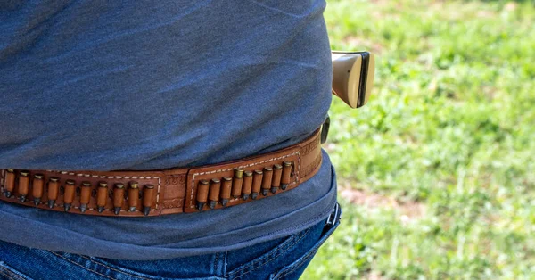 A hand made leather ammo belt is worn around an unidentified man's waist. The loops are filled with 22 shells. Bokeh.