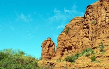 Sarı ve altın renklerinde engebeli dağ oluşumları yeşil bitkilerin saçıldığı canlı mavi gökyüzüne karşıdır..