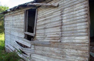 Terk edilmiş bir çiftlik evinin dış duvarındaki çıplak tahtalar bir açıdan görülüyor. Duvarın ortasındaki pencerenin çerçevesi eğiliyor. Bokeh.