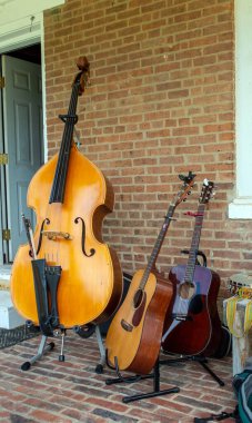Büyük, dik bir bas gitar ve iki gitar açık havada bir tuğla verandada müzisyenlerin başlamasını bekliyor..