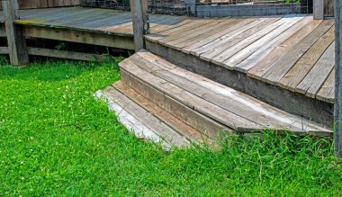 Eski ahşap basamaklar yıpranmış ama yine de güverteye çıkan odak noktası olarak sade bir estetik cazibesi var. Yeşil çimenler doğal hissi över..