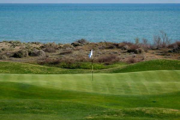 A golf course and its flag pole. Flag pole on a golf green.