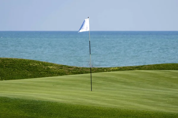 A golf course and its flag pole. Flag pole on a golf green.