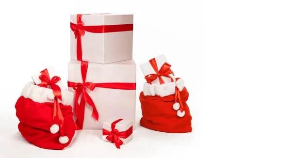 白い紙に包まれ コピースペースのための白いスタジオの背景に赤いリボンで飾られた他のギフトボックスの横にプレゼントでいっぱいのサンタのバッグとクリスマスの背景 — ストック写真