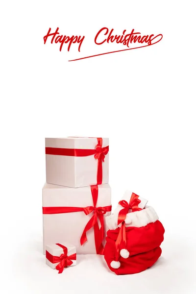 サンタのバッグを他のクリスマスプレゼントの横にクリスマスカード 白い紙に包まれ 赤いリボンで飾られたギフトボックス ハッピークリスマスの碑文と白の背景に垂直形式 — ストック写真