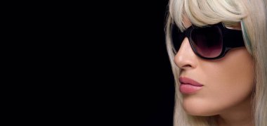 Beautiful young woman with healthy blond hair, wearing black sunglasses. Close-up panorama banner isolated on black background with copy space for text.