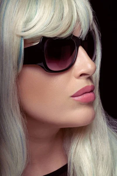 Fashion portrait of an attractive blonde woman with healthy long hair, wearing black sunglasses. Close-up portrait isolated on black background in vertical format