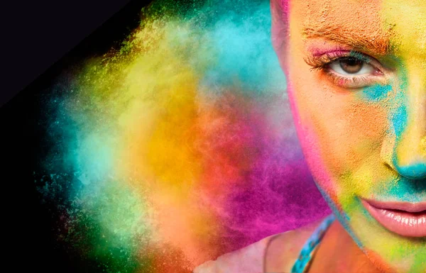 Mysterious young woman covered in rainbow colored powder with a color explosion in the background. Colors Holi festival. Beauty spring concept
