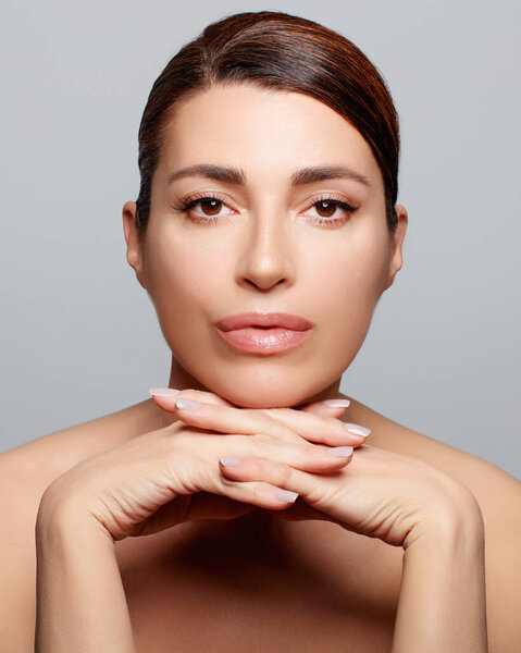 Beauty and skin care concept with a gorgeous brunette woman. Studio portrait on gray background. Vertical format