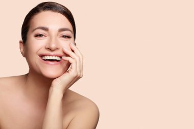 Güzellik ve cilt konsepti. Kusursuz cildinde çıplak makyajla gülümseyen doğal bir kadın. Bej arka planda stüdyo portresi