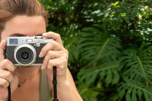 Young woman with a compact camera outdoors taking pictures. Close-up portrait with copy space.