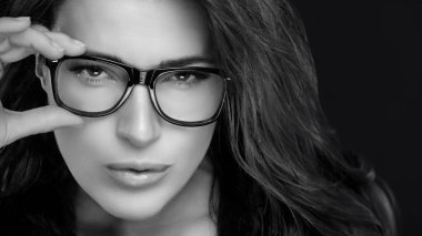 Close up Gorgeous Woman Holding her Eyeglasses While Looking at Camera. Cool Trendy Eyewear Portrait isolated on Black Background