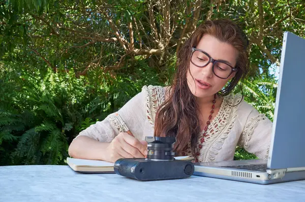 一个戴着眼镜的年轻女人在户外用她的老式笔记本电脑工作 四周环绕着自然 免版税图库照片