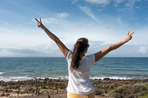 自信的女人做胜利的标志 在海边拥抱健康 富有表现力和享受户外时光 图库照片