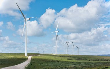 Yeşil alanlar üzerinde yükselen rüzgar türbinlerinin manzarası yenilenebilir enerji ve sürdürülebilirliği simgeliyor.