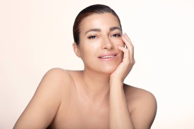 Kusursuz cildi olan, gülümseyen ve rahat, orta yaşlı güzel bir kadın. Güzellik ve cilt reklamları için ideal. Kopyalama alanı olan hafif bir arkaplanda izole edilmiş.