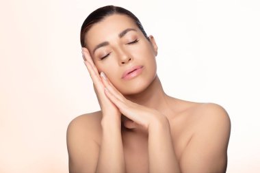 Güzel doğal bir kadın, sakin bir ifadeyle, güzellik ve cilt kavramlarına vurgu yapıyor. Işık arkaplanında kopyalama alanı ile izole edilmiş.